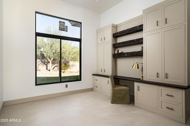 interior space featuring finished concrete flooring, built in desk, and baseboards