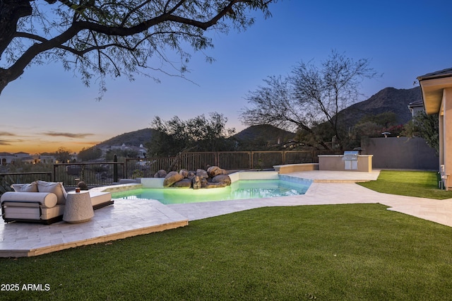 pool at dusk featuring a lawn, area for grilling, a fenced backyard, and a mountain view