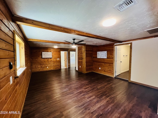 unfurnished living room featuring wood walls, ceiling fan, dark hardwood / wood-style floors, a textured ceiling, and beam ceiling