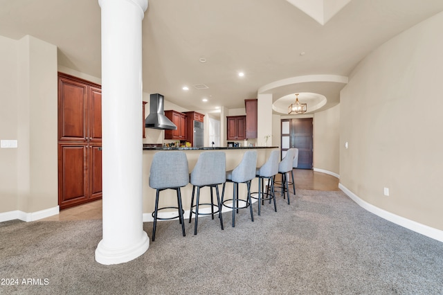 kitchen with kitchen peninsula, light carpet, wall chimney exhaust hood, a breakfast bar, and a chandelier