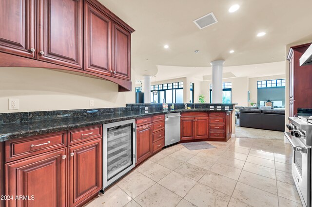 kitchen featuring decorative columns, stainless steel appliances, dark stone counters, beverage cooler, and light tile patterned floors