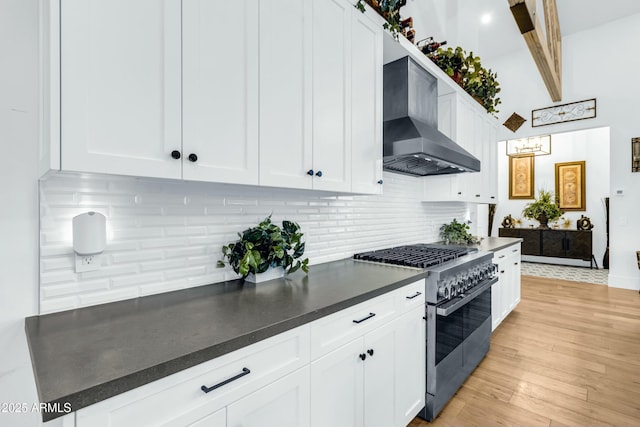 908 W Caldwell St, Phoenix, AZ 85041 - kitchen featuring white cabinets, wall chimney range hood, stainless steel stove, light wood finished floors, and backsplash