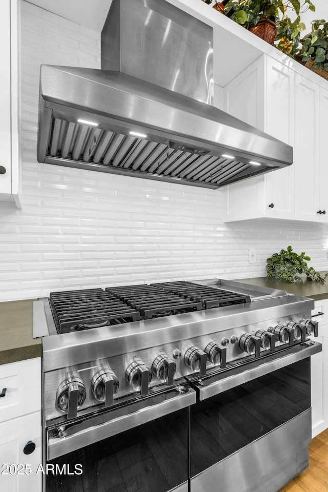 908 W Caldwell St, Phoenix, AZ 85041 - details featuring tasteful backsplash, wall chimney range hood, white cabinetry, dark countertops, and range with two ovens