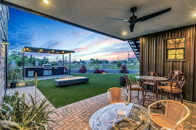 908 W Caldwell St, Phoenix, AZ 85041 - patio terrace at dusk with exterior kitchen, a ceiling fan, outdoor dining area, a fenced backyard, and a lawn