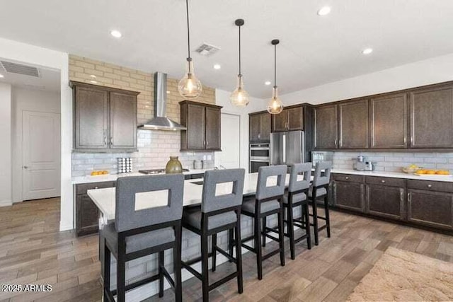 11249 N Blakely St, Surprise, AZ 85388 - kitchen featuring wall chimney exhaust hood, dark brown cabinets, tasteful backsplash, appliances with stainless steel finishes, and recessed lighting