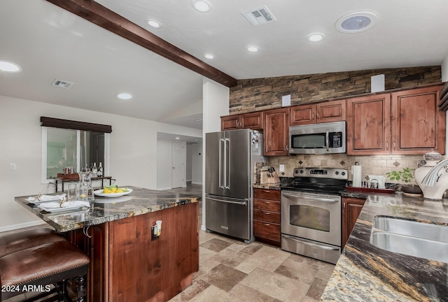 kitchen with a kitchen bar, vaulted ceiling with beams, stainless steel appliances, and dark stone countertops