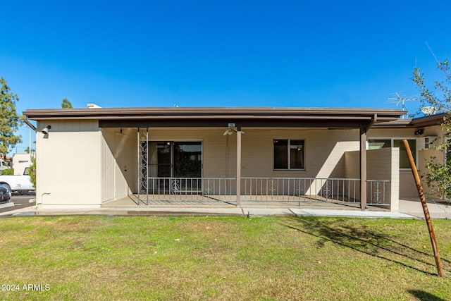 back of property featuring covered porch, ceiling fan, and a lawn