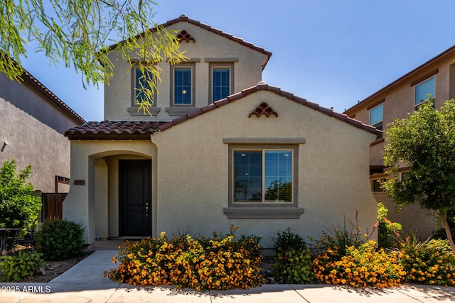 mediterranean / spanish-style house featuring a tile roof, stucco siding, and fence