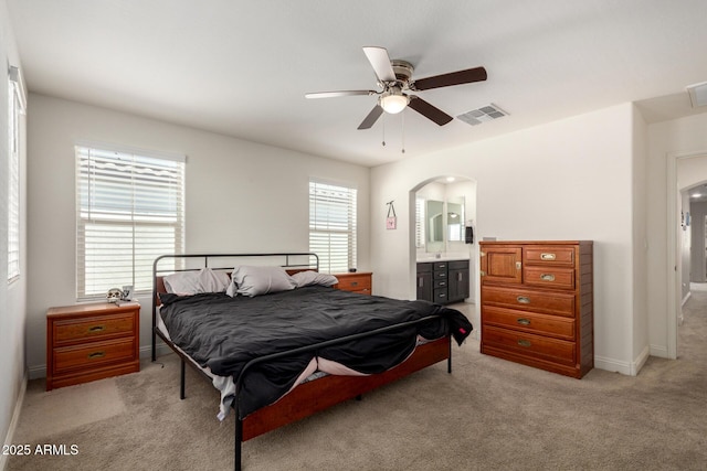 bedroom with arched walkways, light colored carpet, ensuite bathroom, baseboards, and ceiling fan