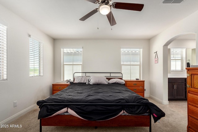 bedroom featuring light colored carpet, arched walkways, multiple windows, and baseboards