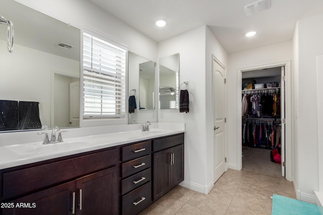 full bathroom featuring tile patterned floors, double vanity, a walk in closet, and baseboards