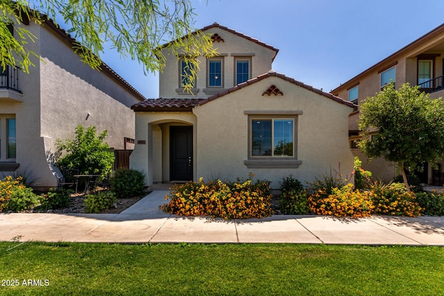 mediterranean / spanish-style home with a tile roof, stucco siding, and a front yard