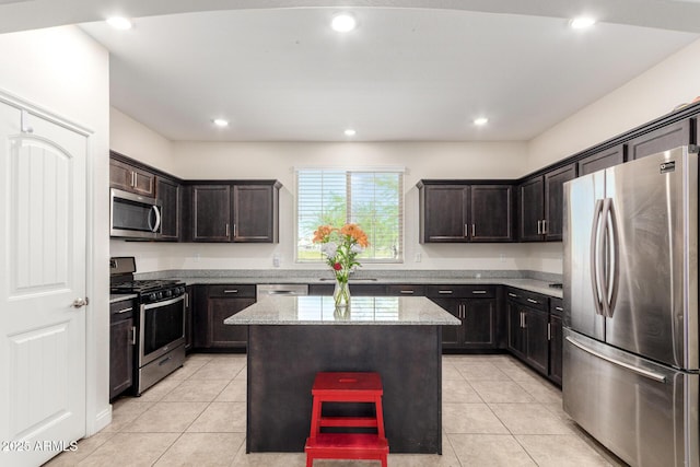 kitchen featuring appliances with stainless steel finishes, light stone counters, light tile patterned flooring, a center island, and dark brown cabinets