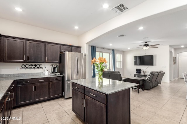 kitchen featuring freestanding refrigerator, arched walkways, light tile patterned floors, a ceiling fan, and dark brown cabinets
