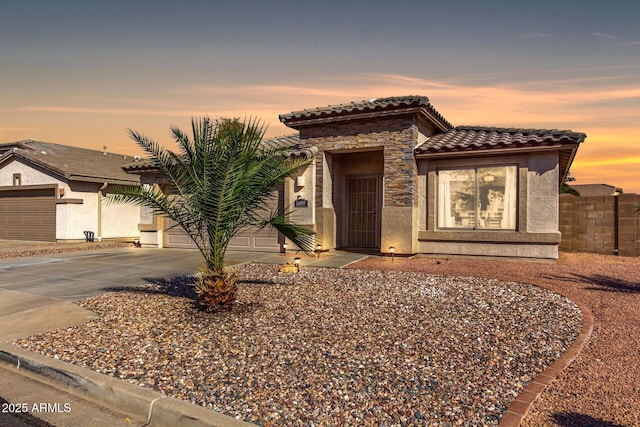 view of front of property featuring a tile roof, stucco siding, concrete driveway, an attached garage, and stone siding