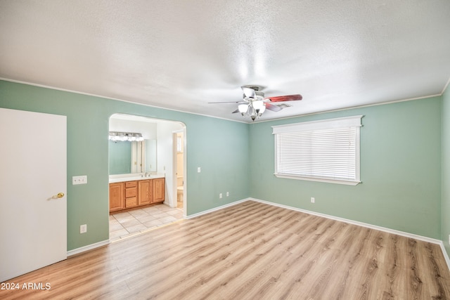 unfurnished bedroom featuring light wood-type flooring, ceiling fan, connected bathroom, ornamental molding, and a textured ceiling