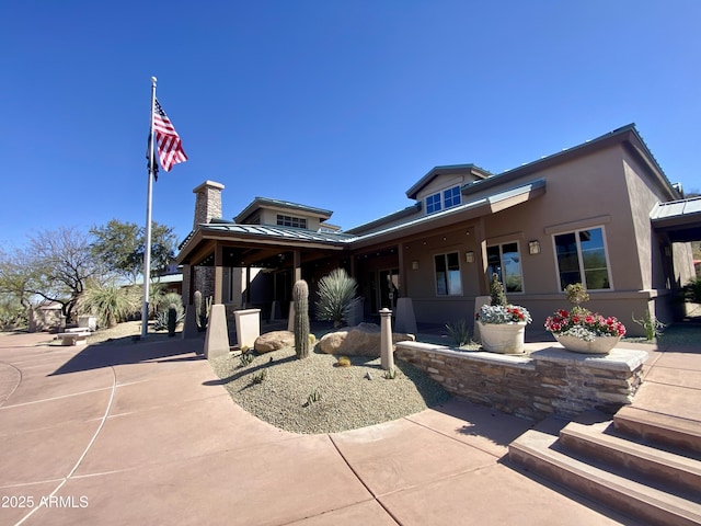 exterior space with a standing seam roof, a chimney, metal roof, and stucco siding