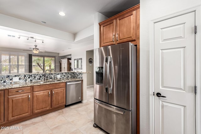 kitchen featuring light stone counters, appliances with stainless steel finishes, brown cabinets, a sink, and backsplash