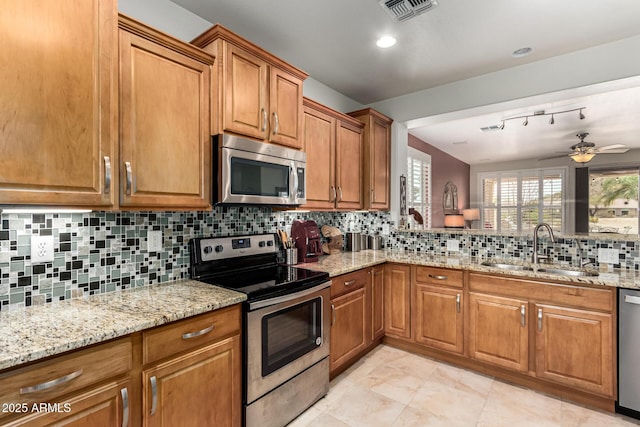 kitchen featuring light stone counters, a sink, visible vents, appliances with stainless steel finishes, and brown cabinetry