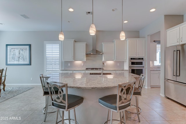 kitchen featuring white cabinets, wall chimney exhaust hood, light stone counters, stainless steel appliances, and a sink