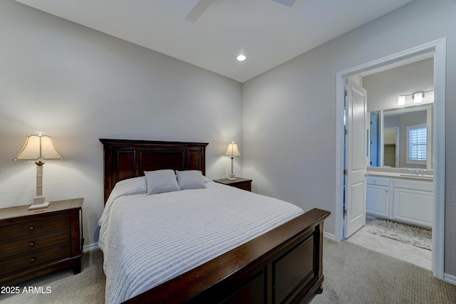 bedroom featuring light carpet, ensuite bath, a sink, and baseboards