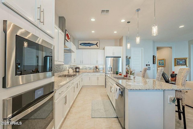 kitchen featuring sink, a kitchen island with sink, white cabinetry, hanging light fixtures, and stainless steel appliances