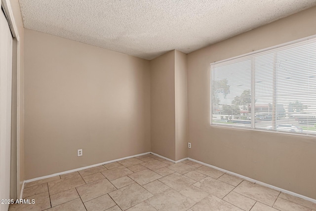 unfurnished room featuring baseboards, light tile patterned floors, and a textured ceiling