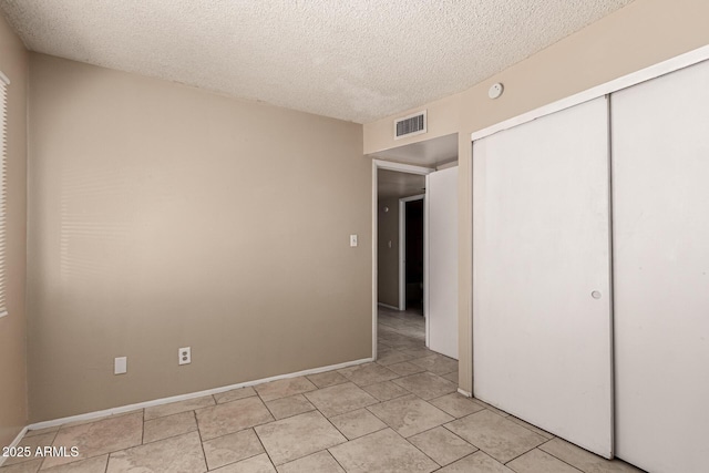 unfurnished bedroom featuring a closet, a textured ceiling, visible vents, and light tile patterned flooring