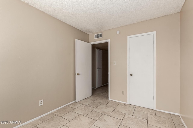 unfurnished bedroom with baseboards, a textured ceiling, visible vents, and light tile patterned flooring