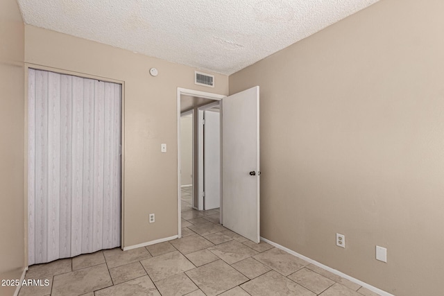 unfurnished bedroom with a closet, a textured ceiling, light tile patterned floors, baseboards, and visible vents
