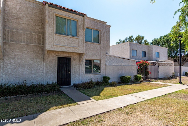 view of front of property with a front lawn, a tile roof, stucco siding, and fence