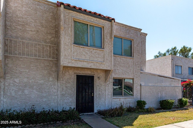 view of front of property with stucco siding, a tile roof, and fence