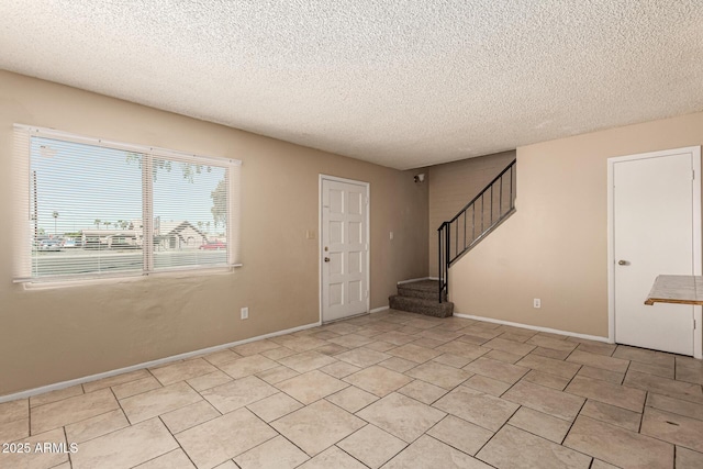 foyer entrance featuring baseboards, stairway, and a textured ceiling