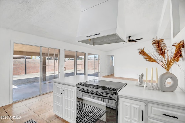 kitchen featuring wall chimney range hood, ceiling fan, black electric range, white cabinets, and light tile patterned flooring