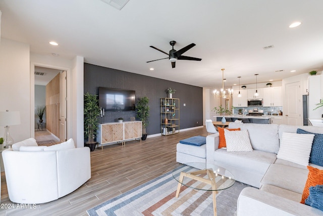 living room with light wood-type flooring and ceiling fan with notable chandelier