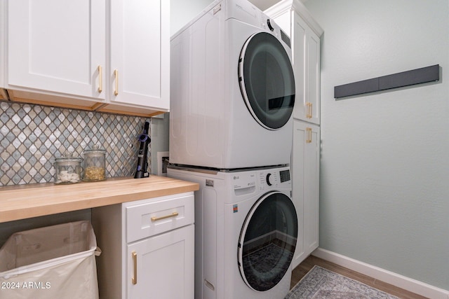 laundry room featuring light wood-type flooring, cabinets, and stacked washer / dryer