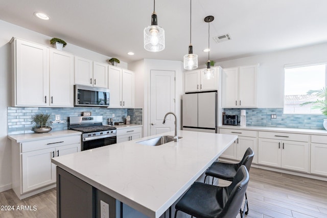 kitchen with backsplash, appliances with stainless steel finishes, white cabinetry, sink, and decorative light fixtures