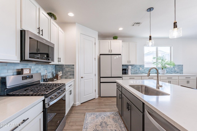 kitchen with sink, appliances with stainless steel finishes, decorative backsplash, light hardwood / wood-style floors, and white cabinets