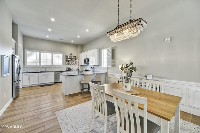 dining space with light wood finished floors, a wainscoted wall, recessed lighting, and a decorative wall