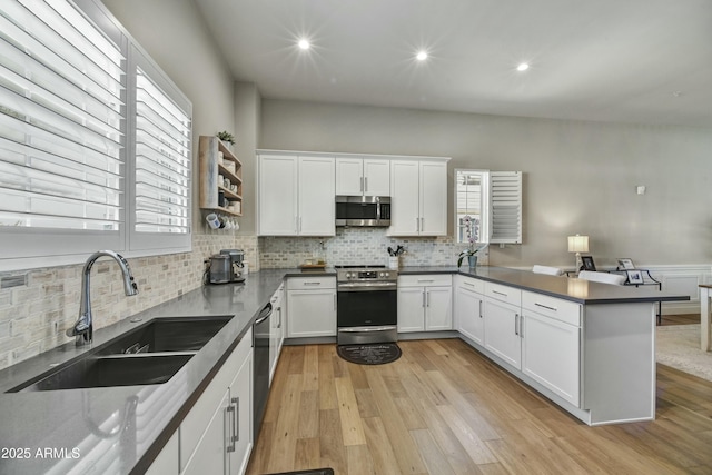 kitchen featuring light wood-type flooring, a peninsula, stainless steel appliances, white cabinetry, and a sink