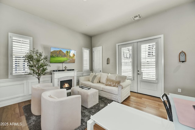 living area featuring visible vents, a wainscoted wall, a warm lit fireplace, wood finished floors, and french doors