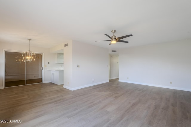 unfurnished living room with ceiling fan with notable chandelier and light hardwood / wood-style flooring