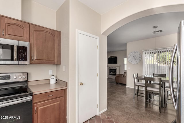kitchen featuring visible vents, arched walkways, a fireplace, light countertops, and stainless steel appliances
