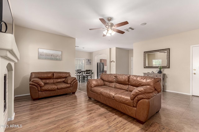 living room with a ceiling fan, arched walkways, visible vents, and baseboards