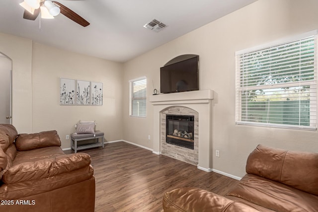 living room with arched walkways, a tiled fireplace, a ceiling fan, wood finished floors, and visible vents