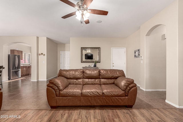living room featuring arched walkways, ceiling fan, baseboards, and dark wood-style flooring