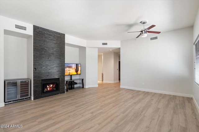 unfurnished living room featuring ceiling fan, a stone fireplace, light wood-type flooring, and heating unit