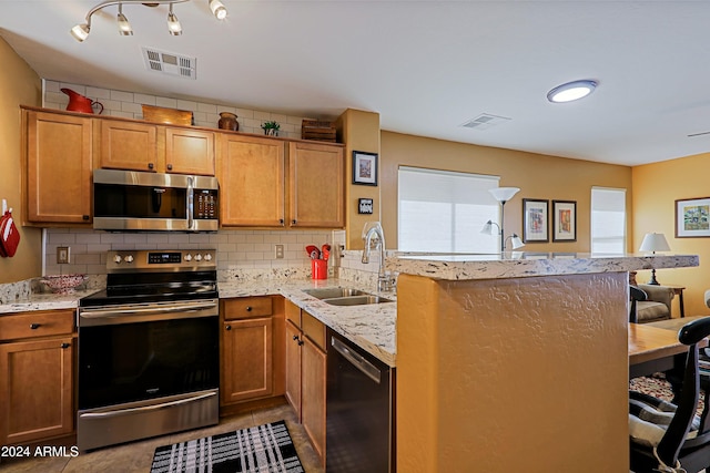 kitchen with stainless steel appliances, light stone counters, kitchen peninsula, sink, and tasteful backsplash