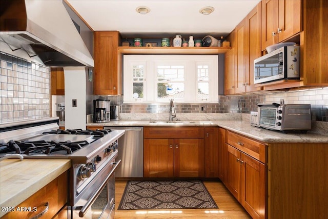 kitchen with sink, wall chimney range hood, tasteful backsplash, appliances with stainless steel finishes, and light wood-type flooring