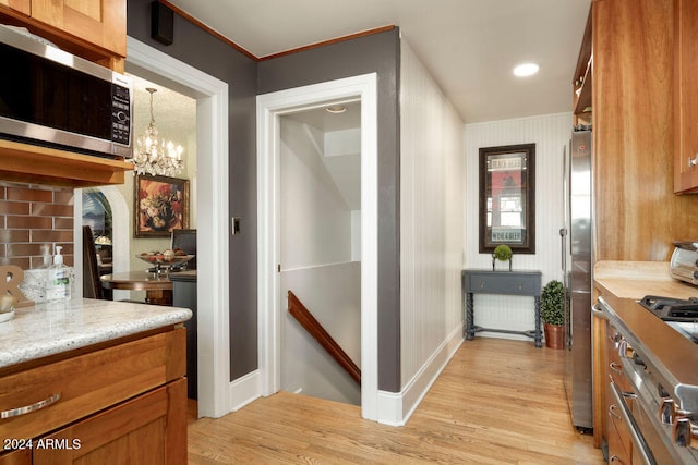 kitchen with an inviting chandelier, light stone counters, decorative backsplash, appliances with stainless steel finishes, and light wood-type flooring